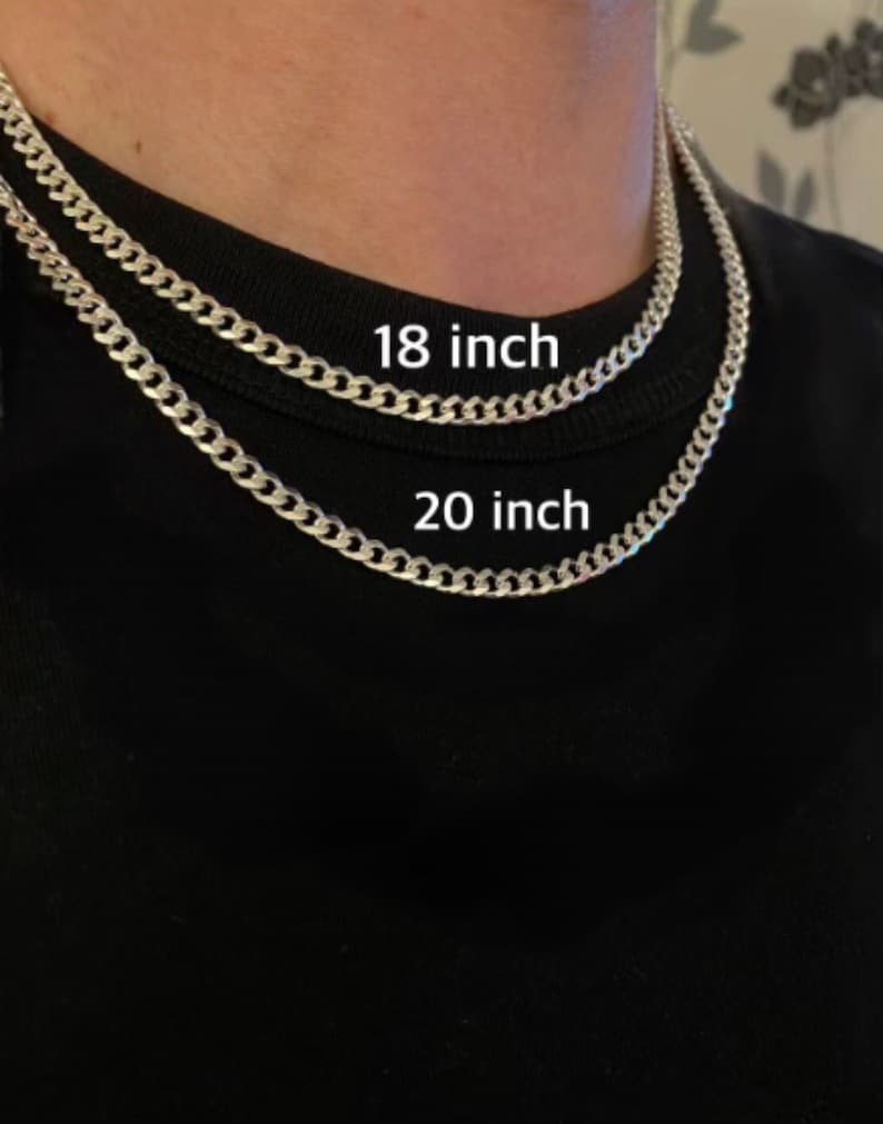 May include: Two silver chain necklaces, one 18 inches long and the other 20 inches long, are shown on a person's neck. The necklaces are both curb chain style.