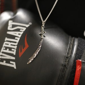 May include: A silver necklace with a detailed sword pendant, resting on a black boxing glove with the word "EVERLAST" printed in white. The glove is partially obscured by a black and white Nike logo.