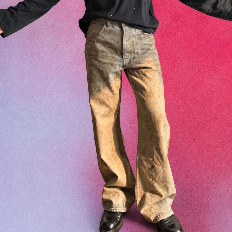 May include: Full-length denim jeans featuring a faded, distressed wash with a gradient transition from grey at the waist to a warm tan and brown tone toward the hem. The jeans have a classic five-pocket construction, a button fly, and a wide-leg cut.