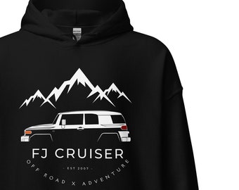 May include: Black hoodie with a white silhouette of a Toyota FJ Cruiser in front of a mountain range. The text "FJ Cruiser - Est. 2007 - Off Road x Adventure" is printed below the vehicle.