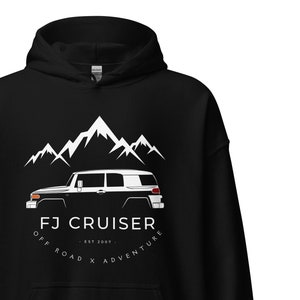 May include: Black hoodie with a white silhouette of a Toyota FJ Cruiser in front of a mountain range. The text "FJ Cruiser - Est. 2007 - Off Road x Adventure" is printed below the vehicle.