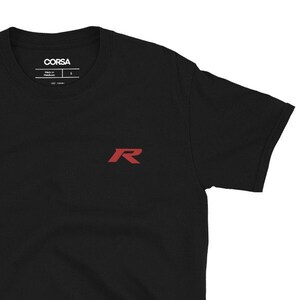 May include: Black short-sleeved t-shirt with a red "R" logo on the front. The logo is a stylized letter "R" with a sharp, angular design. The t-shirt is made of a soft, comfortable fabric.