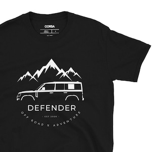 May include: Black t-shirt with a white silhouette of a Land Rover Defender driving through a mountain range. The text "DEFENDER - EST 2020 - OFF ROAD X ADVENTURE" is printed below the vehicle.