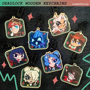Peut inclure: Une collection de huit porte-clés carrés en bois présentant des illustrations de personnages de style anime colorées avec des fermoirs mousquetons en métal noir. Le texte DEADLOCK WOODEN KEYCHAINS et icedaffinity est imprimé en haut.