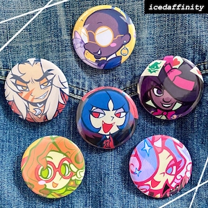 May include: Six circular pin-back badges featuring colourful cartoon character illustrations. The designs include a person with glasses, a long-haired figure, a blue-haired character, a dark-haired figure, a green-haired person, and a pink-haired character. The text icedaffinity is visible in the top right corner.