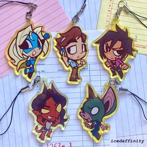 May include: Five acrylic charms with cartoon character designs. The charms feature various characters in different poses and outfits, with a yellow border and a black lanyard. The text "icedaffinity" is visible.