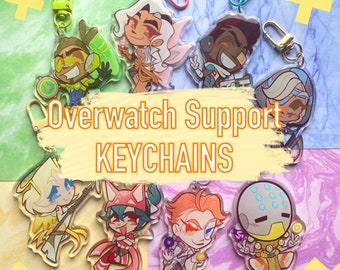 May include: Overwatch Support Keychains featuring various characters from the game. The keychains are made of clear acrylic and feature colorful illustrations of the characters. The characters include Mercy, Moira, Baptiste, Ana, and Zen. The keychains are perfect for any Overwatch fan.
