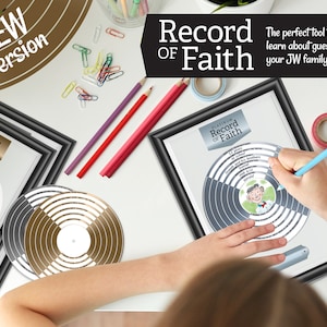 May include: A black framed print featuring a silver record design labelled "Platinum Record of Faith". The record has a central circle with a cartoon illustration of a person. The print is on a white table with a child's hand holding a blue pencil and writing on the record.