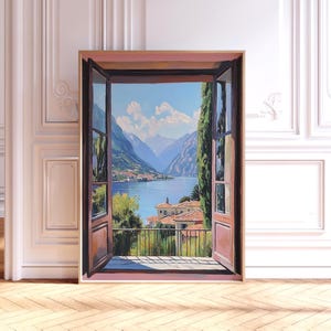以下が含まれることがあります： 開いた窓から見える風景を描いた額入りの絵画。湖、山、建物が描かれています。窓枠は茶色で、空は青く白い雲があります。絵画は静けさを感じさせます。