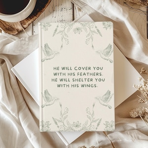 May include: A cream-coloured journal with a green floral design and the text "HE WILL COVER YOU WITH HIS FEATHERS. HE WILL SHELTER YOU WITH HIS WINGS."