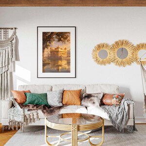 May include: A living room interior with a white couch, a wooden coffee table, a hanging hammock, and a framed print of a golden building reflected in water. The room is decorated with a macrame wall hanging, three woven sunburst mirrors, and a potted plant.