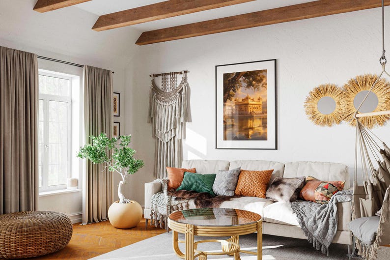 May include: A white couch with a variety of throw pillows in a living room with a wooden ceiling, a large window with beige curtains, a potted plant, a coffee table with a glass top, and a wall hanging.