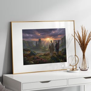 Op de afbeelding: Een ingelijste landschapskunstafdruk met een gouden lijst. Het kunstwerk toont twee figuren in gewaden die naar een zonsondergang over een bergachtig landschap lopen. De lucht is gevuld met dramatische wolken en het terrein is weelderig.
