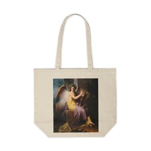 Puede incluir: Bolso tote beige con una pintura clásica de una figura alada con una corona de laurel y vestida con túnicas amarillas y moradas. La figura está sentada y escribe en una tableta. El bolso tiene asas largas.