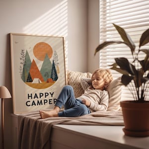 Puede incluir: Una impresi&oacute;n art&iacute;stica enmarcada con un tema de camping, con un sol, monta&ntilde;as y &aacute;rboles, con el texto "HAPPY CAMPER". Una persona descansa en un asiento junto a la ventana, con una planta en una maceta de terracota en primer plano.