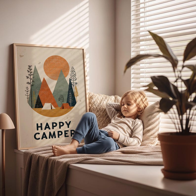 Puede incluir: Una impresi&oacute;n art&iacute;stica enmarcada con un tema de camping, con un sol, monta&ntilde;as y &aacute;rboles, con el texto "HAPPY CAMPER". Una persona descansa en un asiento junto a la ventana, con una planta en una maceta de terracota en primer plano.