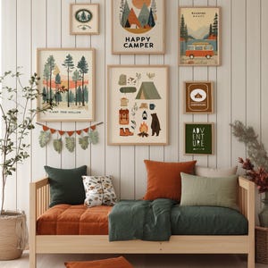 Puede incluir: Una escena de dormitorio acogedora con un sof&aacute; cama de madera con ropa de cama y cojines naranjas y verdes. Encima, arte enmarcado con tem&aacute;tica de camping con textos como "Happy Camper" y "Adventure Awaits" decora la pared. Una alfombra tejida y plantas en macetas completan el espacio acogedor.