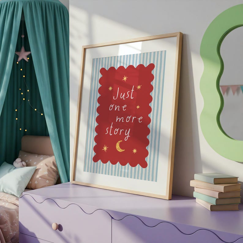 A framed poster with a red background and a blue and white striped border, displaying the text "Just one more story" in a whimsical font. The poster is placed on a purple dresser, with a stack of books and a green mirror visible in the background.
