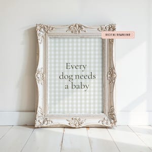 May include: A framed print with the text "Every dog needs a baby" in a decorative, ornate, off-white frame. The background of the print has a light green and white gingham pattern. A small pink rectangle in the upper right corner reads "DIGITAL DOWNLOAD."