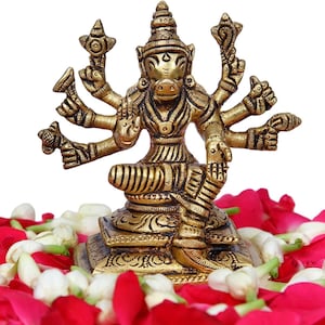 May include: A detailed brass statue of a multi-armed deity with a boar-like head, seated on a decorative base. The statue is golden in color and is surrounded by red rose petals and white flowers, creating a vibrant contrast against the white background.