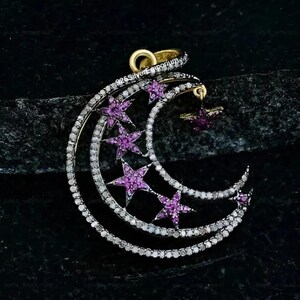 Può includere: Un ciondolo a forma di mezzaluna con un design a doppio strato incastonato con piccole pietre bianche e accentuato da cinque pietre rosa a forma di stella. Un piccolo ciondolo a stella pende dalla curva interna. Il testo 925SilverEmporium è visibile.