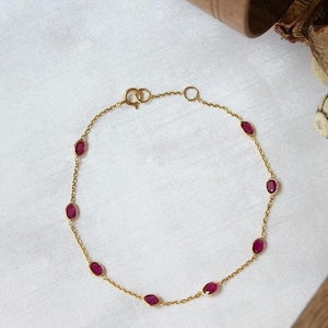 Könnte beinhalten: Ein goldenes Kettenarmband mit ovalen roten Edelsteinen.