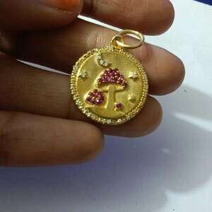 Peut inclure: Pendentif doré avec un motif de champignon. Le pendentif présente un champignon central avec un chapeau en pierres précieuses rouges et un champignon plus petit en dessous. Il est entouré de petites pierres blanches et possède une boucle pour une chaîne.