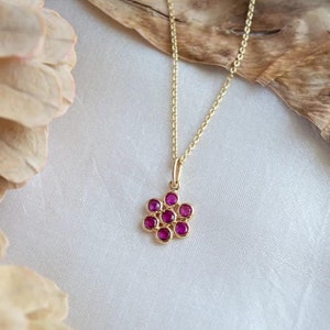 Könnte beinhalten: Eine goldene Kettenkette mit einem Anhänger, der aus einer Gruppe kleiner, runder, rosafarbener Edelsteine besteht, die in Gold gefasst sind.