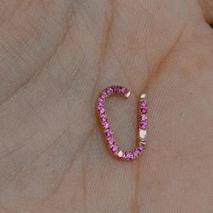Può includere: Un orecchino a cerchio in oro con pietre preziose rosa. Il cerchio ha la forma di una U ed è progettato per essere indossato nella parte superiore dell'orecchio.