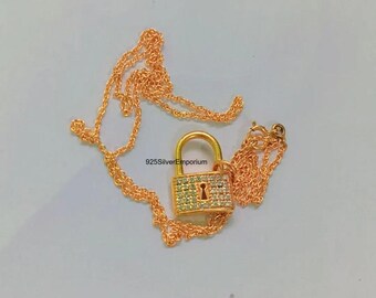May include: A gold-toned necklace featuring a padlock pendant encrusted with small clear stones and a central keyhole cutout. The chain is delicate and link-style. The text 925SilverEmporium is printed near the padlock pendant on the surface.