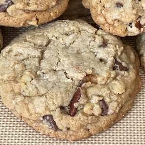 May include: Close-up of a large, golden brown chocolate chip cookie with pecans and a slightly crispy texture.