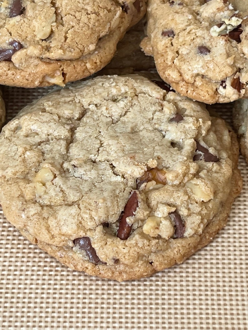 May include: Close-up of a large, golden brown chocolate chip cookie with pecans and a slightly crispy texture.