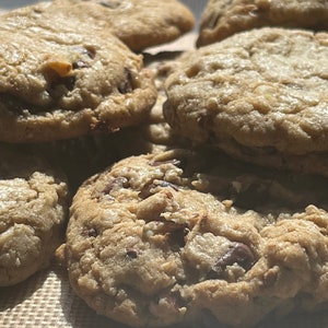 May include: A close-up of a batch of freshly baked chocolate chip cookies on a brown baking sheet.