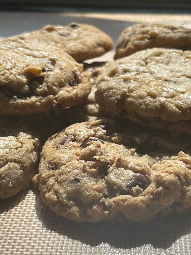 May include: A close-up of a batch of freshly baked chocolate chip cookies on a brown baking sheet.