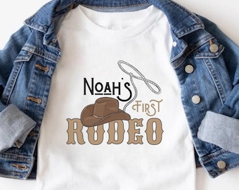 Pode incluir: Camiseta branca com um chapéu de cowboy marrom e o texto "Noah's First Rodeo" em letras marrons.