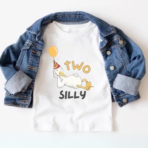 May include: White t-shirt with a cartoon duck wearing a party hat and holding a balloon. The text "two silly" is printed below the duck.