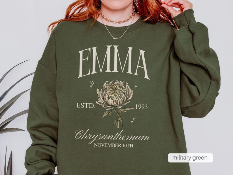 Peut inclure: Un sweat-shirt vert militaire avec le nom "EMMA" imprim&eacute; en blanc, un graphique de chrysanth&egrave;me et le texte "ESTD. 1993 Chrysanthemum NOVEMBER 10TH".