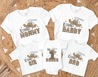 Pode incluir: Um conjunto de cinco t-shirts brancas com designs de chapéus de cowboy marrons e texto. As t-shirts dizem "Rodeo Mommy", "Rodeo Daddy", "Rodeo Sis", "My 1st Rodeo" e "Rodeo Bro".
