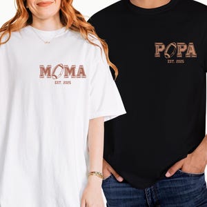 May include: Two t-shirts, one white and one black, with a football graphic and the text "MOMA EST. 2005" on the white shirt and "PAPA EST. 2005" on the black shirt.