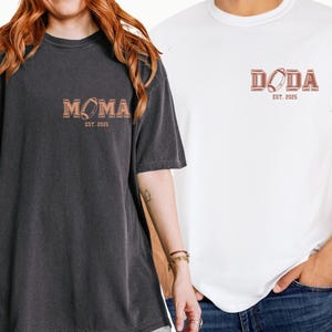 May include: Two t-shirts, one black and one white, with a football graphic and text. The black shirt says "MOMA EST. 2025" and the white shirt says "DODA EST. 2025".