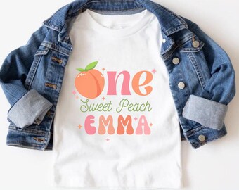 Peut inclure: T-shirt blanc avec un graphique de pêche et le texte "one sweet peach EMMA".