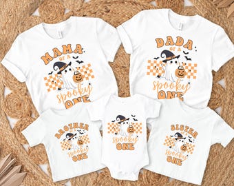May include: Set of five white t-shirts with a Halloween theme. The shirts feature a ghost wearing a witch hat and holding a pumpkin. The text on the shirts reads "Mama of a Spooky One", "Dada of a Spooky One", "Brother of a Spooky One", "Sister of a Spooky One", and "Spooky One".