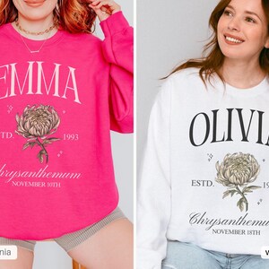 Peut inclure: Deux sweat-shirts rose et blanc avec un motif floral et du texte. Le sweat-shirt rose a le texte "EMMA ESTD. 1993 Chrysanthemum NOVEMBER 10TH" et le sweat-shirt blanc a le texte "OLIVIA ESTD. 1997 Chrysanthemum NOVEMBER 18TH".