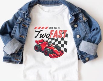 May include: White t-shirt featuring a red race car graphic and the text "THIS BOY IS TWO FAST". A blue denim jacket is draped over the shirt. The design includes a checkered flag.