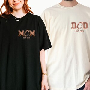 May include: Two t-shirts, one black and one ivory, with a football design and the words "MOM EST. 2025" and "DAD EST. 2025" printed on them.