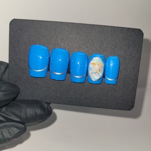 May include: Set of six blue press-on nails with a silver accent and a single nail featuring a cherub design.