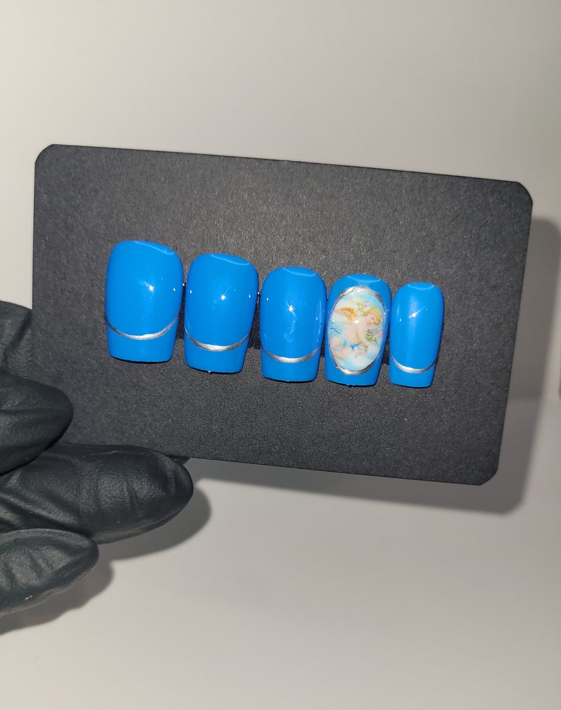 May include: Set of six blue press-on nails with a silver accent and a single nail featuring a cherub design.