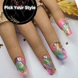 May include: Close-up of four long, pink and green iridescent nails with a swirl design. The nails are on a hand with a gold ring.