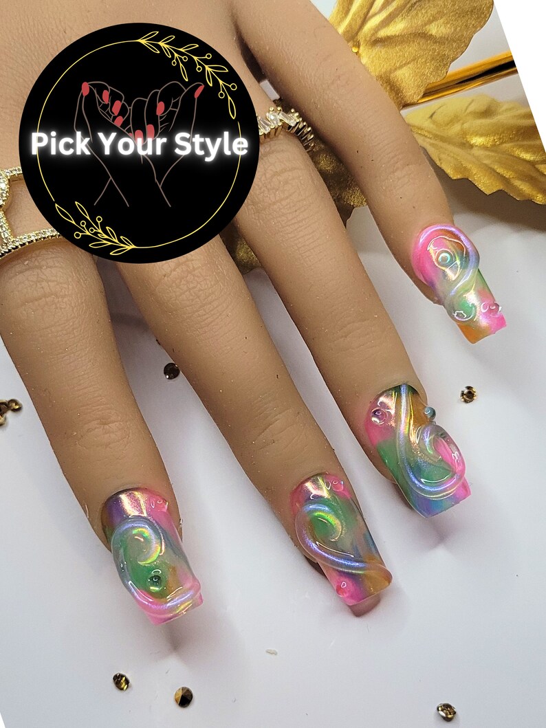 May include: Close-up of four long, pink and green iridescent nails with a swirl design. The nails are on a hand with a gold ring.