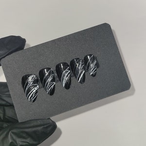 May include: Set of six black and white false nails with a white swirl design.
